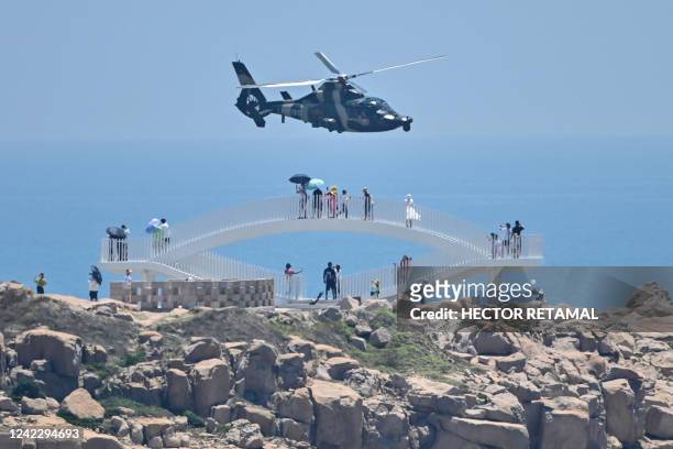 Tourists look on as a Chinese military helicopter flies past Pingtan island, one of mainland China's closest point from Taiwan, in Fujian province on...