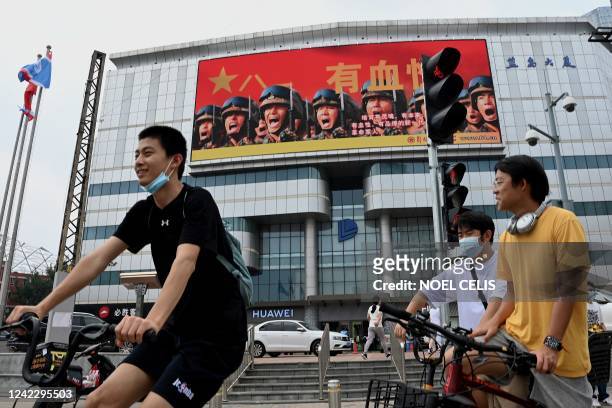 Large screen on a building showing promotion for the Chinese People's Liberation Army is seen past cyclists in Beijing on August 4, 2022. - China's...