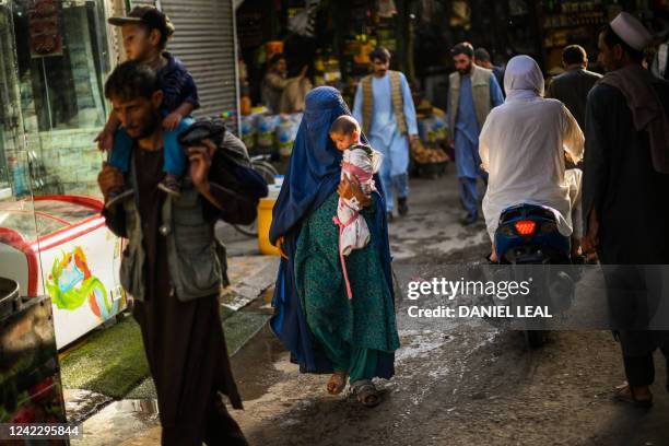 In this picture taken on July 20 a woman wearing a traditional burqa and carrying a child walks through a market in Kabul.