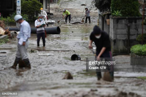 People clean up a road in a residential area after heavy rains and mud covered a road in the town of Oe, Yamagata Prefecture, on August 4, 2022....