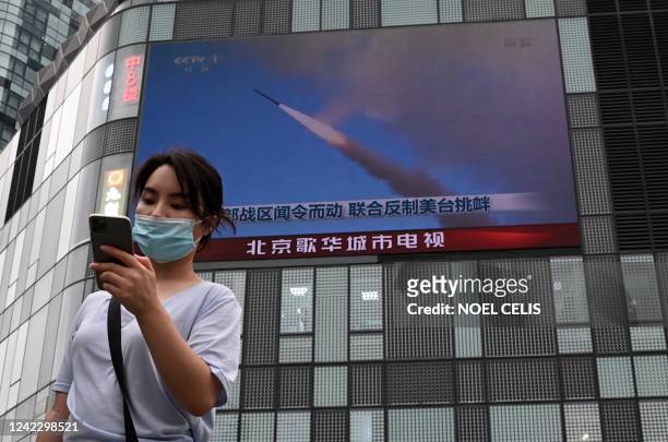 Woman uses her mobile phone as she walks in front of a large screen showing a news broadcast about China's military exercises encircling Taiwan, in...