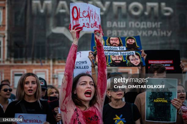 Woman with fake blood stains brandishes a paper reading "Olenivka" during a protest of friends and relatives of Azov battalion servicemen of...