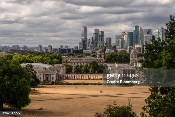 Parched grass in Greenwich Park in front of a view of skyscrapers in the Canary Wharf financial, business and shopping district, in the Greenwich...