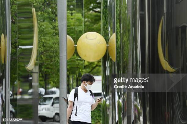 Man using his smartphone walks by an art exhibit on the street in Hiroshima, Japan on August 5, 2022. The city of Hiroshima will commemorate the 77th...