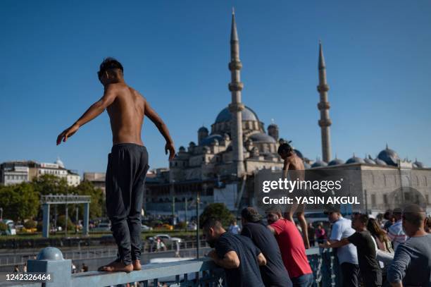 Two young men ready to dive into the waters of the Bosphorus from the Galata Bridge to cool down, in Istanbul on August 5, 2022.