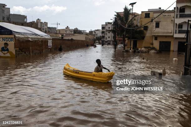 Young boy pushes his inflatable canoe down a flooded road after heavy rains in Dakar on August 5, 2022.