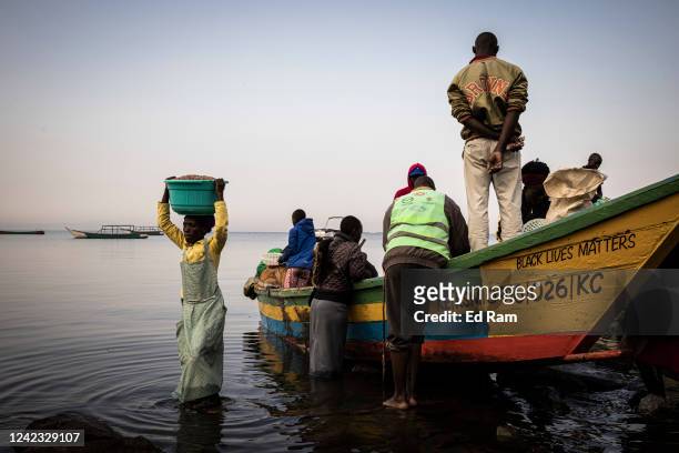 People buy fish as boats arrive at a dock on the edge of Lake Victoria at dawn, on August 5, 2022 in Kisumu, Kenya. The fishing industry, which has...