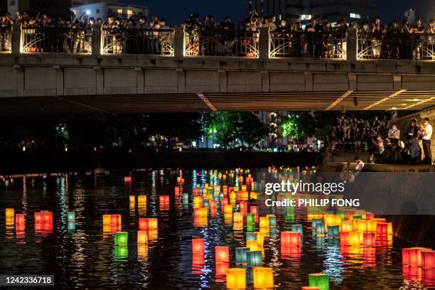 People watch paper lanterns floating on the Motoyasu River beside the Hiroshima Prefectural Industrial Promotion Hall, commonly known as the atomic...