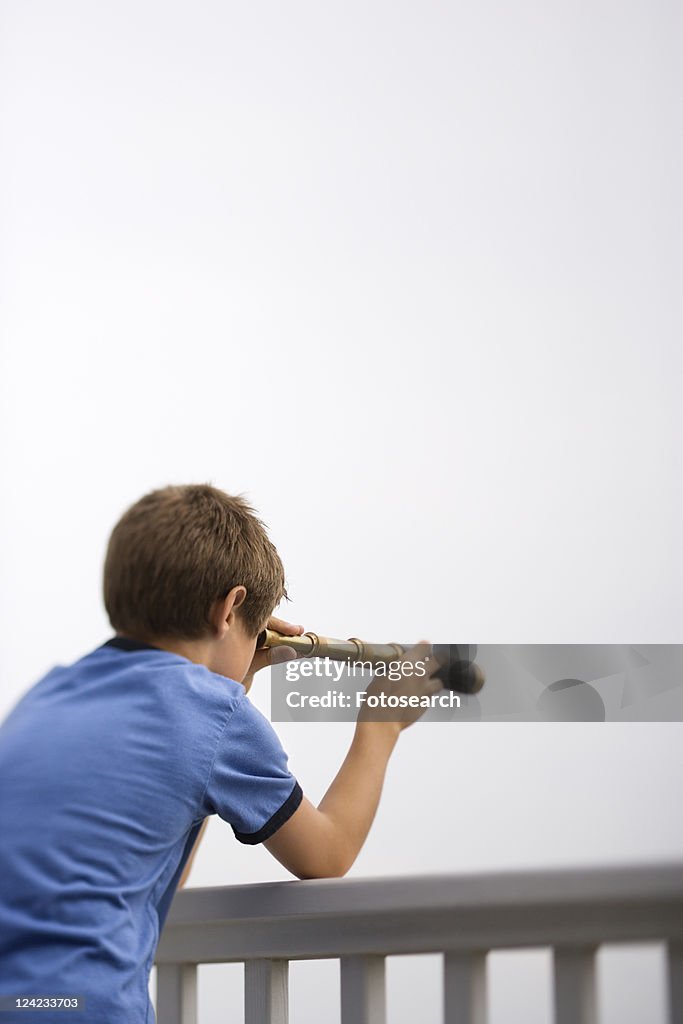 Caucasian pre-teen boy leaning on railing looking through telescope.