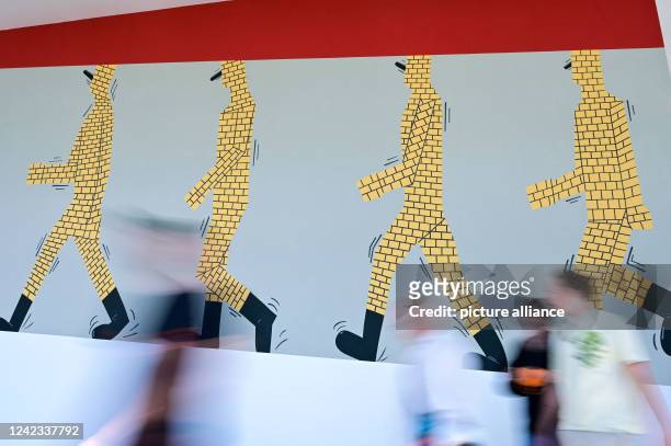 August 2022, Hessen, Kassel: Visitors to documenta fifteen walk past a mural by the Instituto de Artivismo Hannah Arendt collective from Havana in...