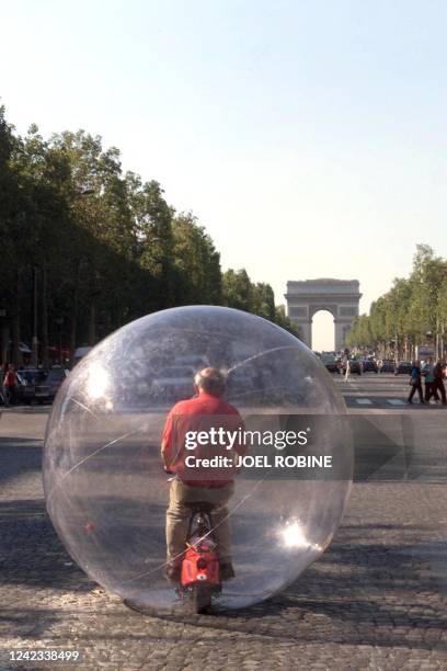 L'architecte américain Hans Walter Muller roule, le 22 septembre sur les Champs Elysées à Paris, sur un vélo électrique dans une bulle de plastique...