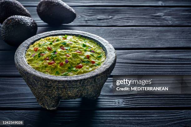 guacamole avocado mexican recipe in stone molcajete on black wood background - guacamole stock pictures, royalty-free photos & images