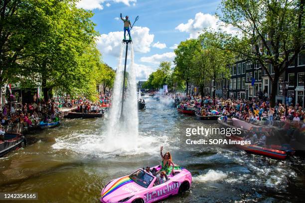 Man is seen flying over the water while cheering the public. The Canal Parade is what Amsterdam Gay Pride is famous for. It's the crown on their two...