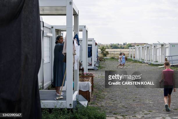 Migrant hangs laundry under the entrance porch as other walk past the container-accommodations at the former Tempelhof Airport in Berlin, Germany, on...