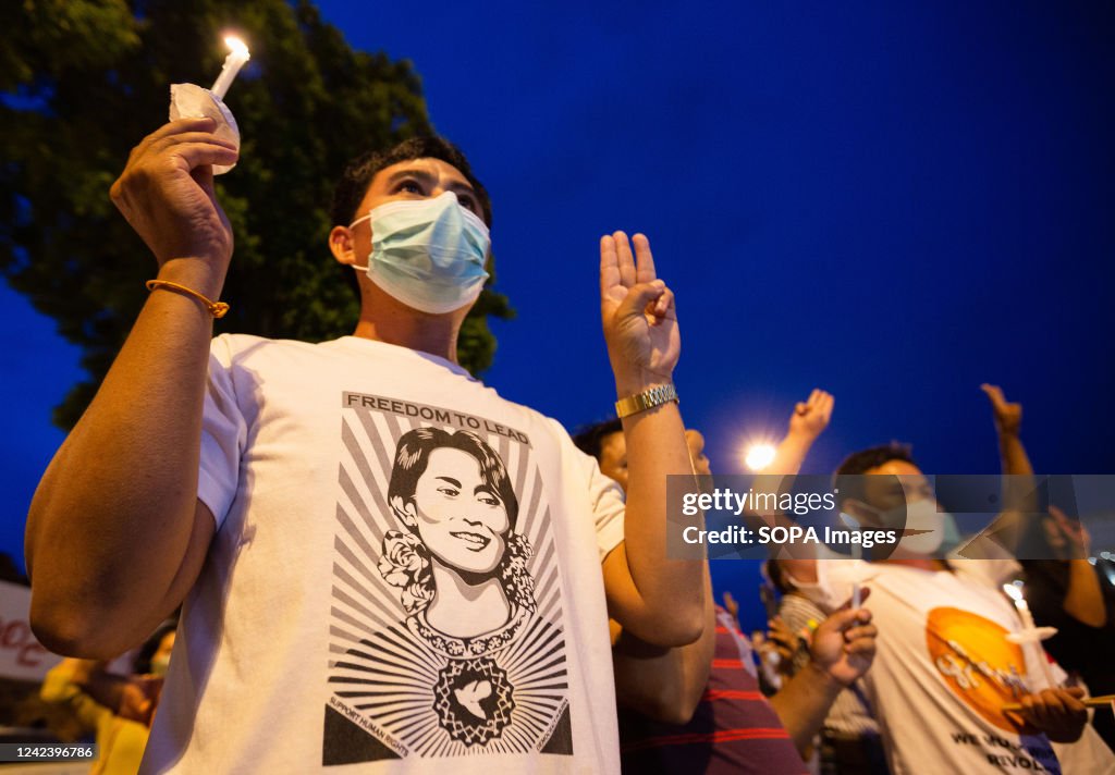 Activists hold candles and raise three finger salutes during...