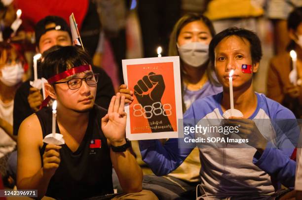 An activist holds a lit candle and raises three finger salutes during the anniversary of the '8888 Uprising' at Tha Phae Gate in Chiang Mai. On the...