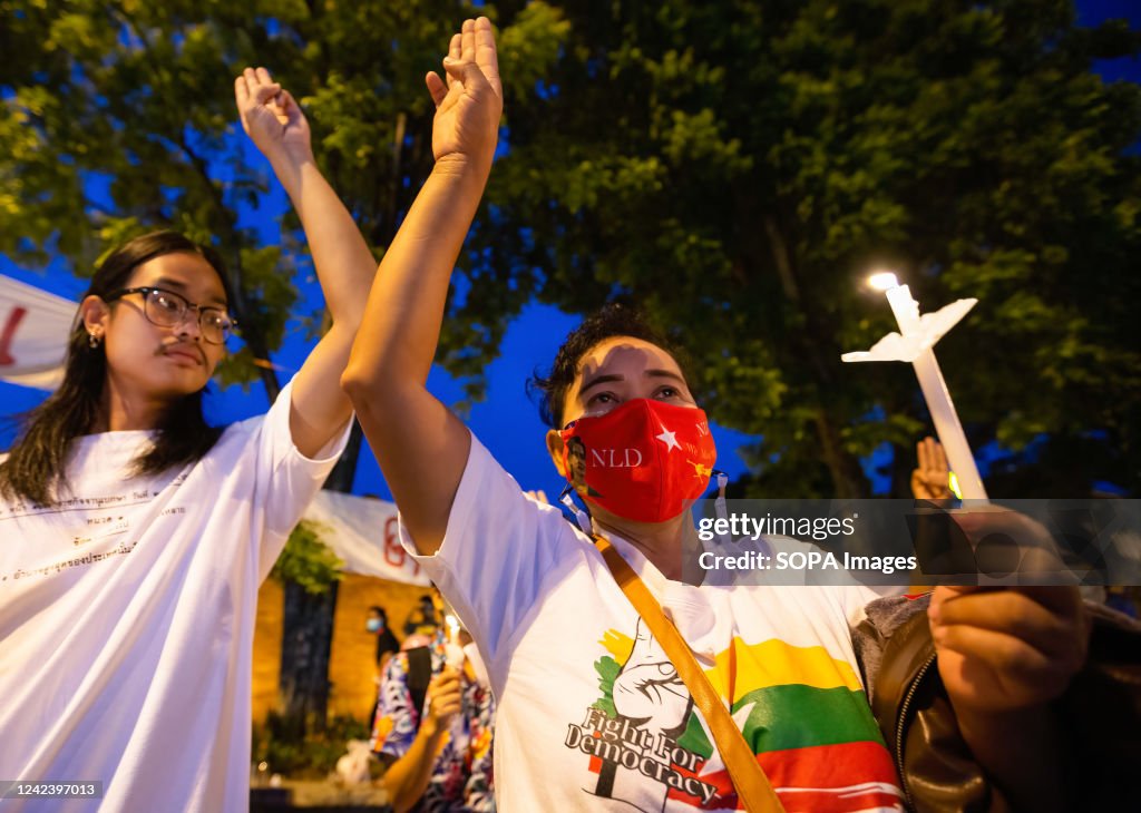 An activist holds a lit candle and makes a three-finger...