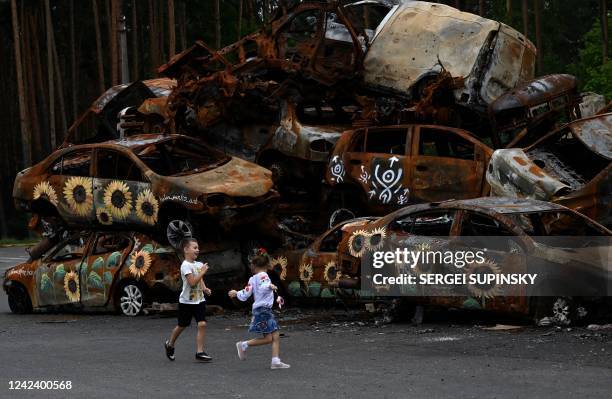 Children play at the symbolic cemetery of cars shot by Russian troops , some painted by local artists, in Irpin, on August 9 amid Russian invasion of...