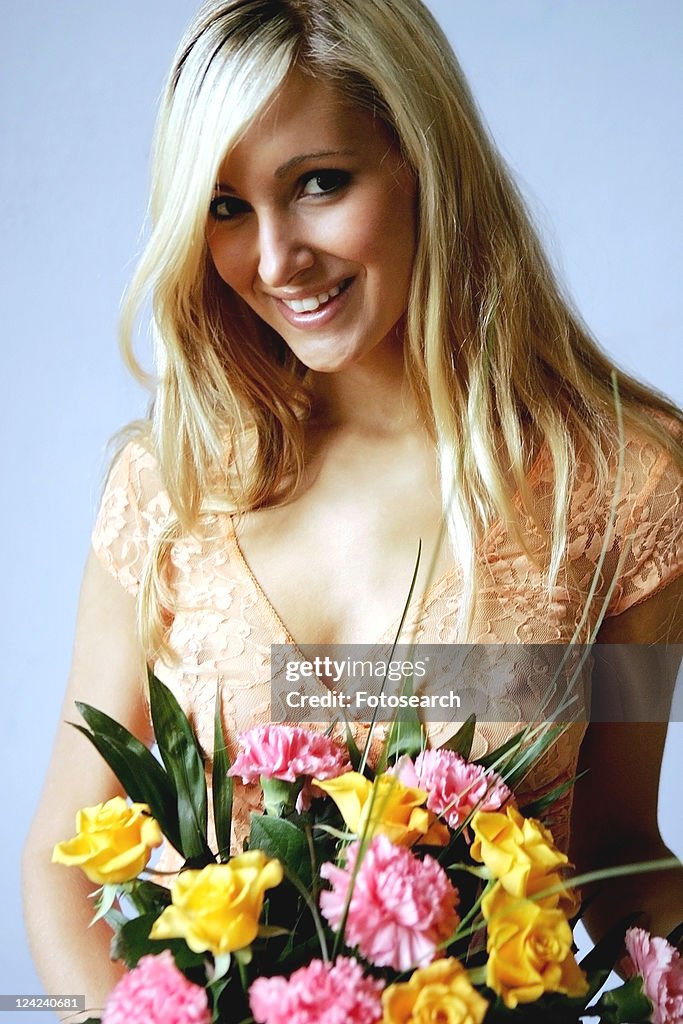 Young woman in see-through top holding bouquet of flowers, smiling