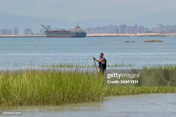 Man paddles past reeds as the Xiamen city skyline on the Chinese mainland is seen from Taiwan's Kinmen islands, which lie just 3.2 kms from the...