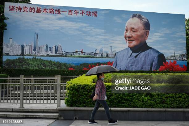 This photo taken on July 13, 2022 shows a woman walking past a billboard of former Chinese leader Deng Xiaoping in Shenzhen, China's southern...