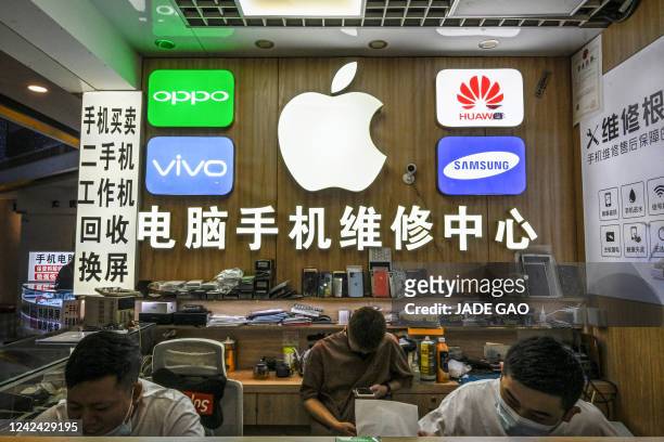 This photo taken on July 12 shows staff members working at a store with logos of phone manufacturers including Apple, Huawei, Oppo, Vivo and Samsung,...