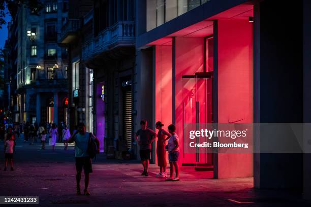 Pedestrians outside an illuminated Nike Inc. Store, ahead of the start of new rules requiring businesses to turn off lighting at night, in Barcelona,...