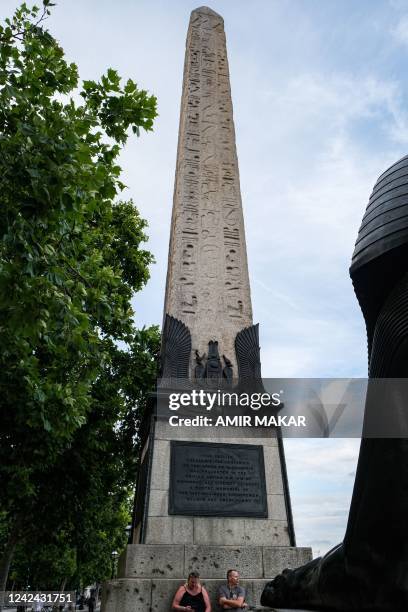 People sit beneath the ancient Egyptian Obelisk of Thutmose III , known as "Cleopatra's Needle", along the Thames river embankment in London on July...