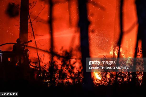 Firefighter sprays water towards flames at a wildfire near Belin-Beliet, southwestern France, overnight on August 11, 2022. - French officials warned...