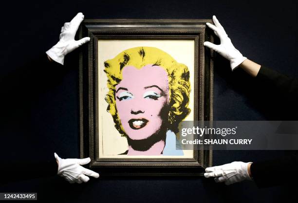 Two Christie's employees hold a painting called 'Lemon Marilyn' by Andy Warhol, dated 1962, during an Impressionist and Modern Art showcase press...