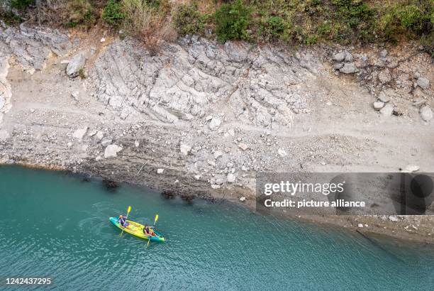 August 2022, France, Aiguines: Two vacationers paddle a canoe into the Verdon Gorge at the Lac de Sainte-Croix reservoir at low water. Heat and lack...