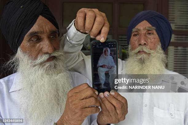 In this picture taken on August 3 Baldev Singh and his brother Gurmukh Singh display a picture of their sister Mumtaz Bibi on a mobile phone in...