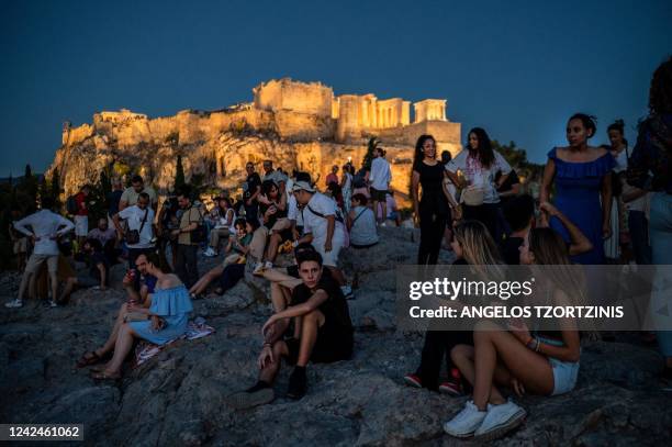 Tourists visit the Areios Pagos hill, with the Acropolis' Propylaea seen in the background, in Athens on August 12, 2022.