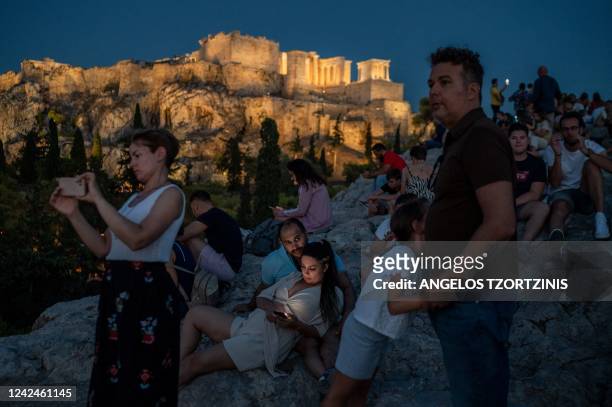 Tourists visit the Areios Pagos hill, with the Acropolis' Propylaea seen in the background, in Athens on August 12, 2022.