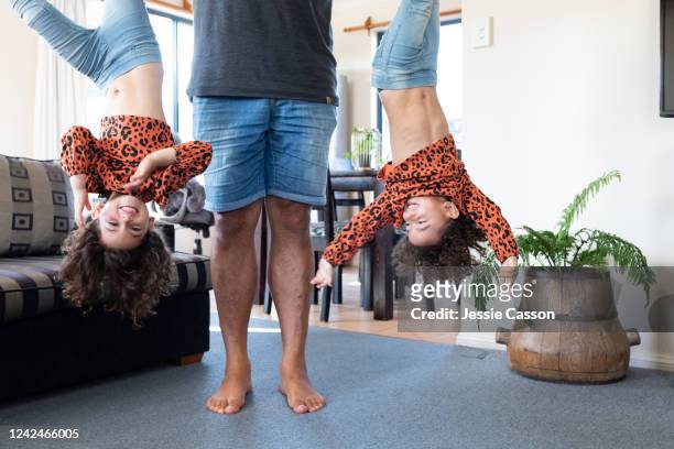 a father holds his twin daughters upside down - twin stock pictures, royalty-free photos & images