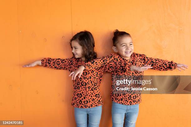 twin sisters with matching outfits having fun standing in orange background - matching outfits stock pictures, royalty-free photos & images