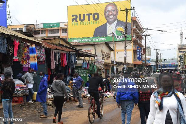 Pedestrians walk in a street next to a billboard of Kenya's Deputy President William Ruto and presidential candidate for the United Democratic...
