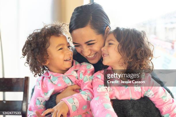 happy embrace between mother and twin daughters in pyjamas - cute twins stock-fotos und bilder