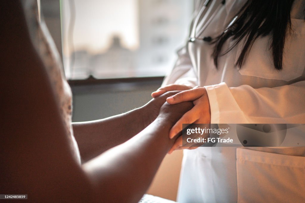 Vrouwelijke arts die handen van haar patiënt bij het ziekenhuisruimte houdt