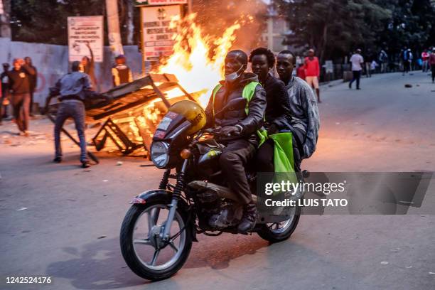 Motorcycle driver and his two passangers leave the area during riots in front a burning barricade in front of Kenyan Police Officers in the informal...