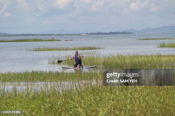 This picture taken on August 10, 2022 shows tourist Joseph Lin practicing stand up paddling in the waters on the Kinmen islands with a view of Xiamen...
