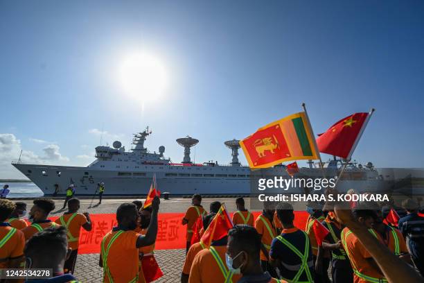 Workers wave China's and Sri Lanka's national flags upon the arrival of China's research and survey vessel, the Yuan Wang 5 at Hambantota port on...