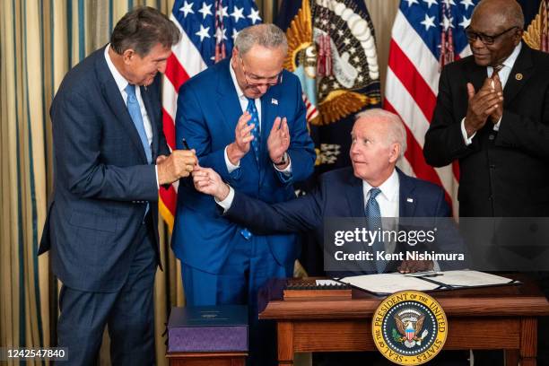 President Joe Biden, center, hands the pen used to sign H.R. 5376, the Inflation Reduction Act of 2022 into law, to Sen. Joe Manchin in the State...