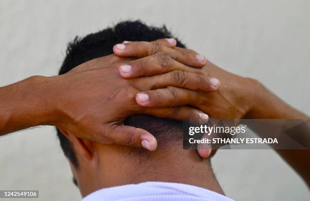 Young man being questioned by a police officer holds his hands on the back of his head during a security operation against gang violence in...