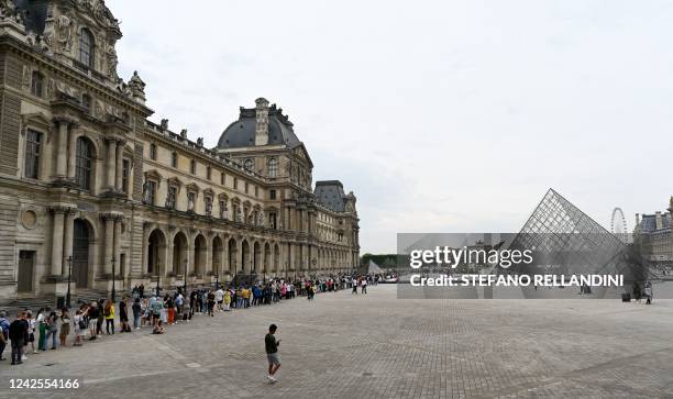 Visitors queue in front of the Louvre's Pyramide, designed by Ieoh Ming Pei, to visit the Louvre museum in Paris on August 17, 2022. - RESTRICTED TO...