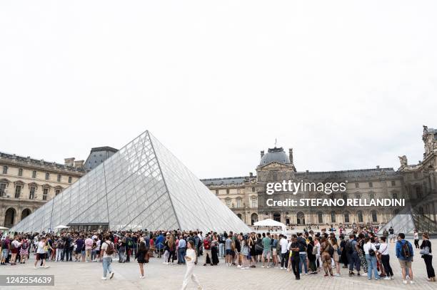 Visitors queue in front of the Louvre's Pyramide, designed by Ieoh Ming Pei, to visit the Louvre museum in Paris on August 17, 2022. - RESTRICTED TO...