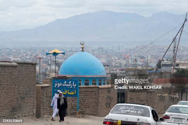 Afghan men walk past the blue dome of a mosque a day after the blast in the outskirts of Kabul on August 18, 2022. - The death toll from a blast...