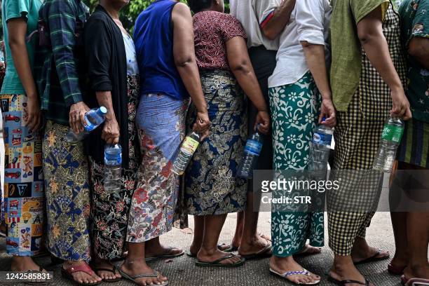 People queue with empty plastic bottles to buy cheap vegetable oil, in Yangon on August 18, 2022. - Dozens queued under monsoon drizzle for...