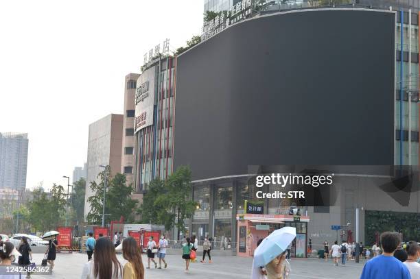 This photo taken on August 17, 2022 shows people walking past a screen which is shut down to save energy in Chengdu, in China's southwestern Sichuan...