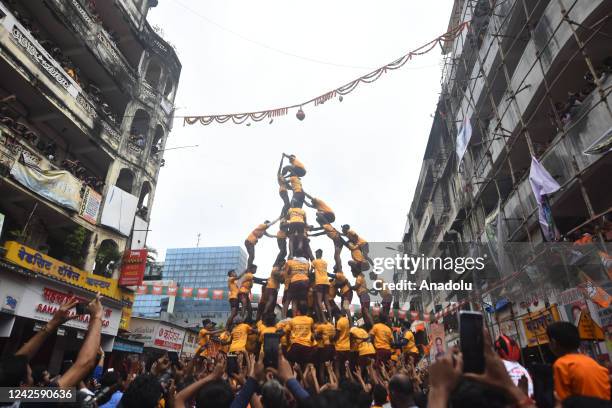 Indian young Hindu devotee hangs from a rope after breaking a dahi-handi suspended in the air as a human pyramid collapses beneath him during...